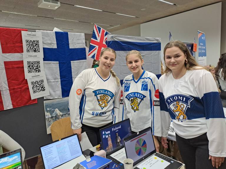Three students with Finland-shirts on standing next to each other.