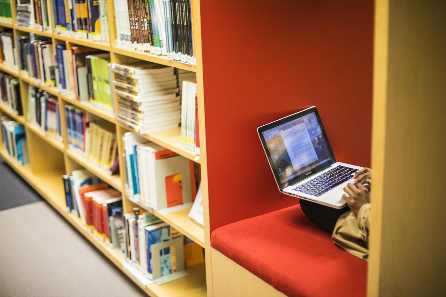 Opiskelija kirjastossa tietokoneen kanssa.