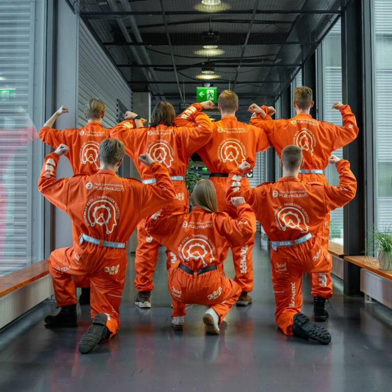 Opiskelijoita poseeraa oransseissa haalareissa.