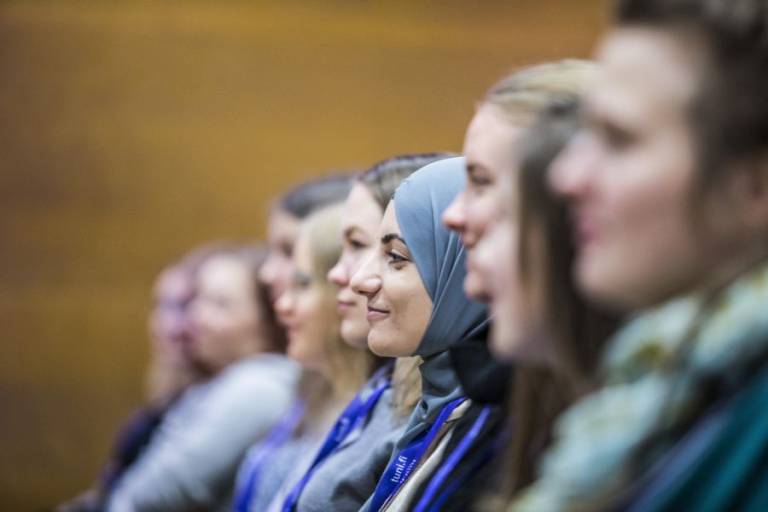 Opiskelijat istuvat luentosalissa ja katsovat hymyillen eteenpäin.