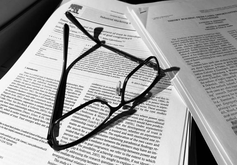 Tieteellisen artikkelin päällä mustasankaiset silmälasit.