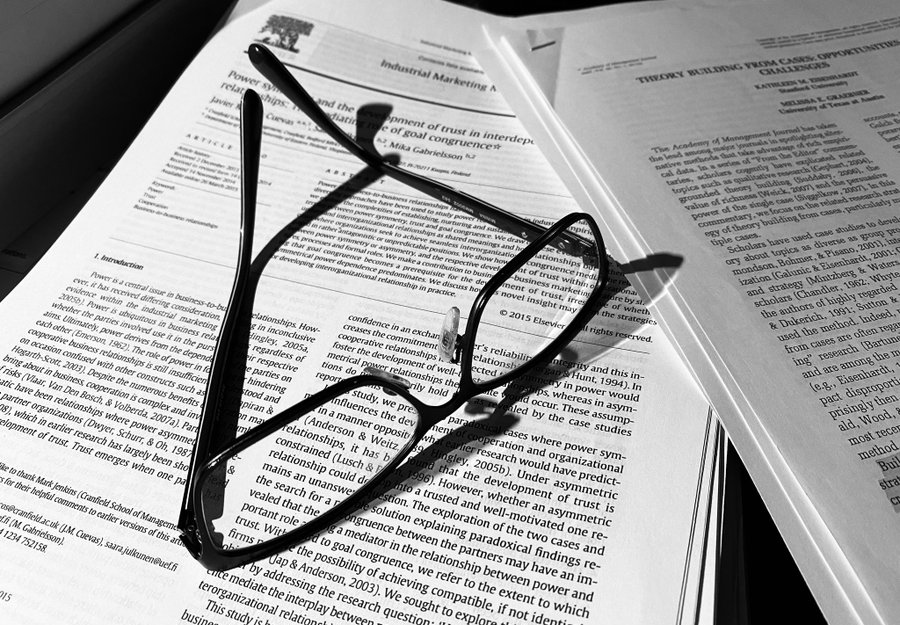 Tieteellisen artikkelin päällä mustasankaiset silmälasit.