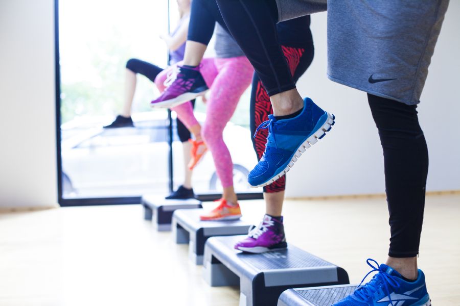 Ihmisiä seisomassa steppilautojen päällä ryhmäliikuntatunnilla.