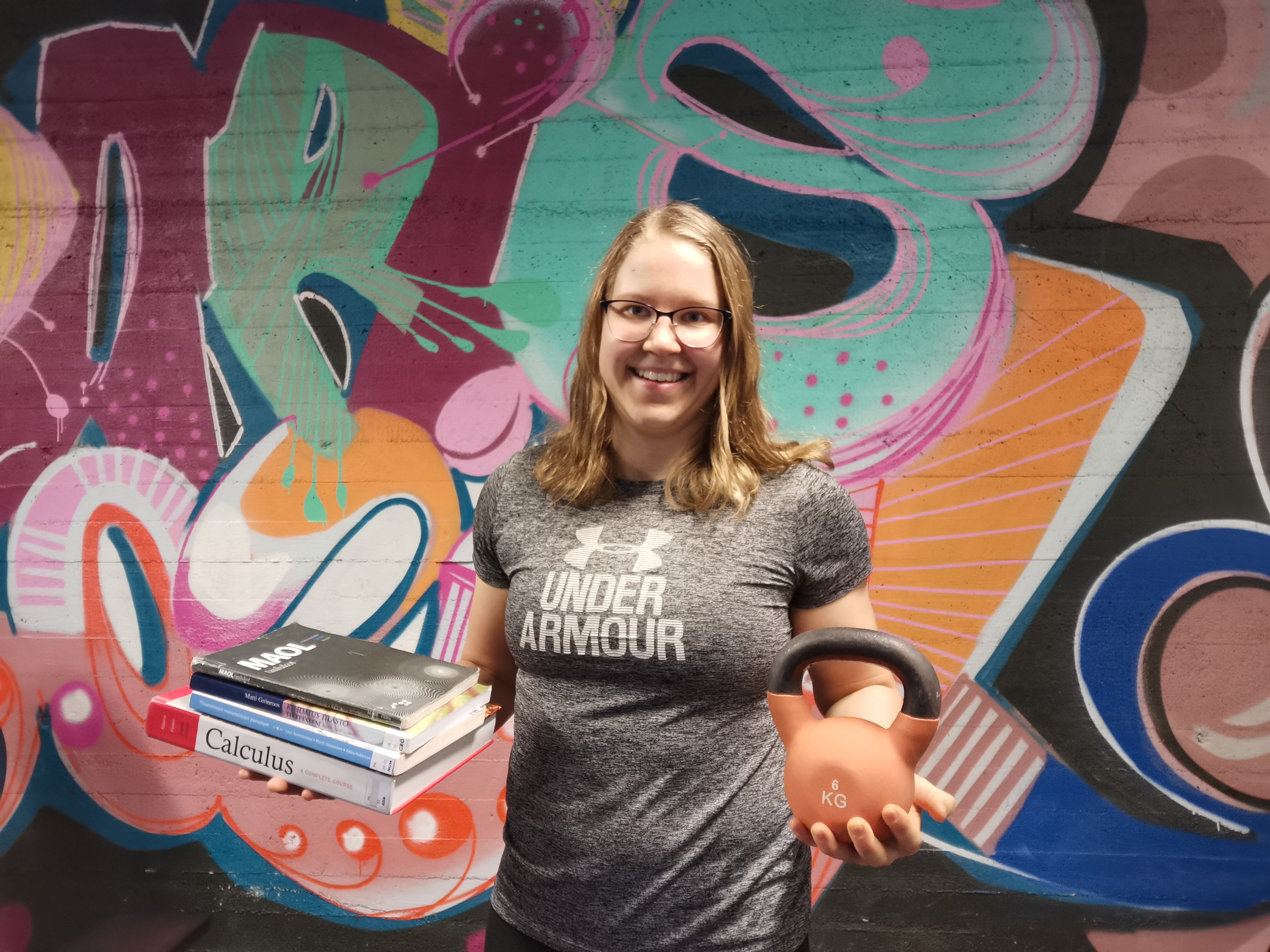 Johannalla toisessa kädessä kirjoja ja toisessa kahvakuula.