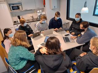 Opiskelijat istuvat pöydän ääressä tietokoneiden kanssa yhdessä