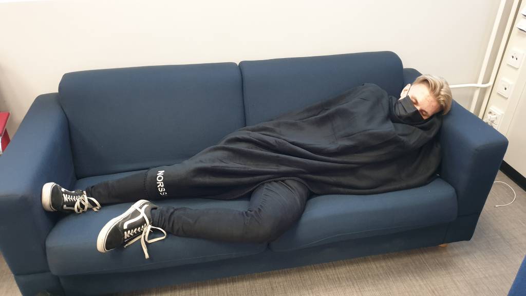 Opiskelija nukkuu sohvalla viltin alla Tampereen norssin lukiossa.