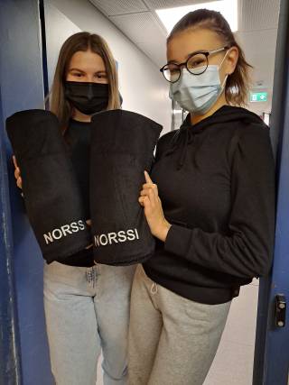 Kuva, jossa kaksi tyttöä näyttää saamiaan Norssi-vilttejä, eli mustia vilttejä, joissa lukee Norssi