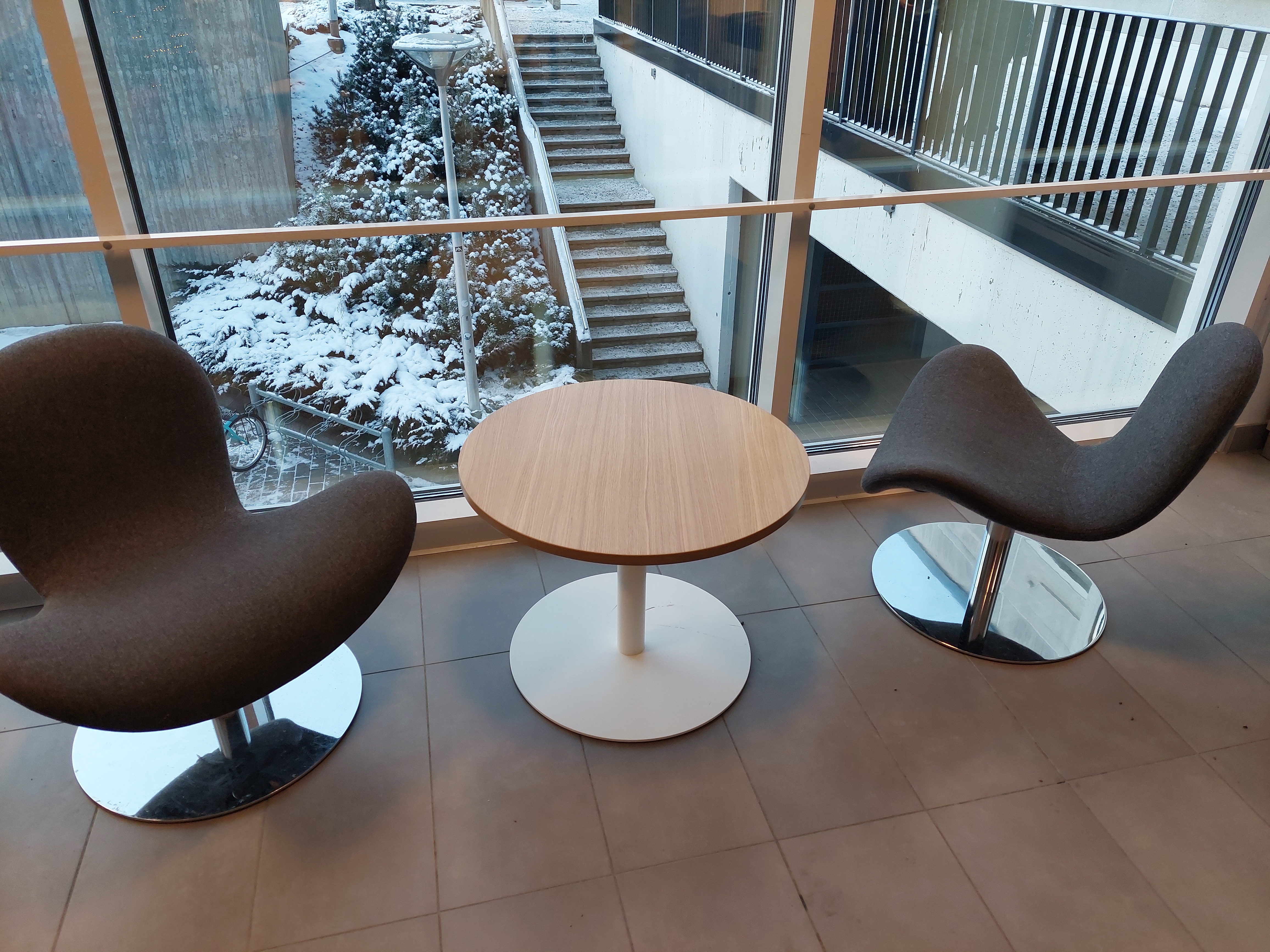 Kuva, jossa kaksi tuolia ja pyöreä pieni pöytä isojen ikkunoiden edessä.