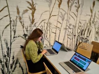 Kuva, jossa henkilö työskentelee kannettavan tietokoneen kanssa istuen pöydän ääressä-