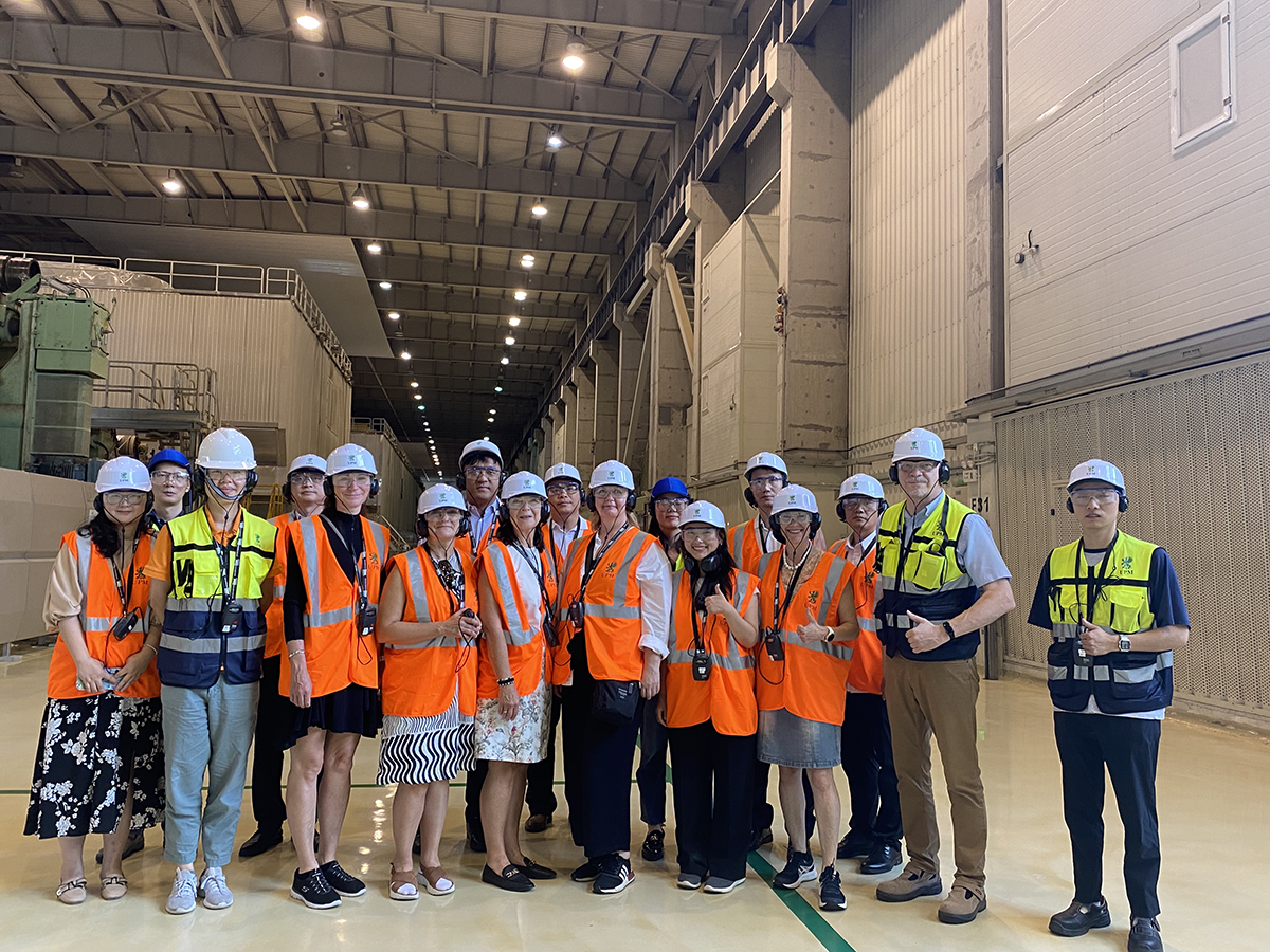 Seventeen people standing in a group with helmets and reflective safety vests on.