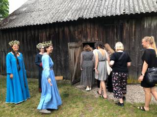 Henkilöitä menossa perinteiseen puiseen taloon, tanssijoita perinnepuvuissa.