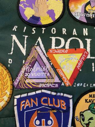 Kaksi Kolmiot-haalarimerkkiä omeltuna opiskelijahaalareihin. Text: Kolmiot 20 vuotta.