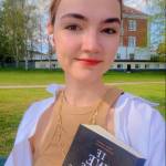 Anastasia, the author, is taking a selfie and is holding a book.