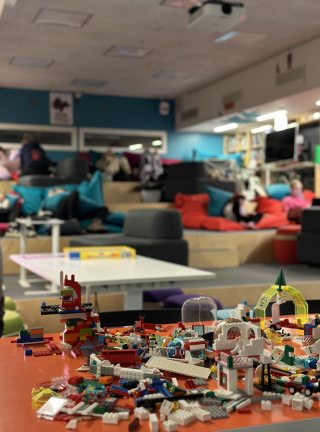 Play space OASIS. Legos on a table in the foreground. People working or playing in the background.