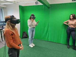Kolme opiskelijaa testaavat VR-laseja vihreän virtuaaliseinän edessä.