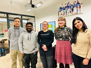 Four university students with their thesis supervisor. All are looking and smiling to the camera. There is a sign that says "Robostudio" behind them.