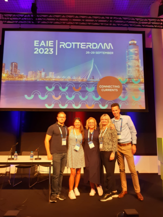 Viisi ihmistä seisoo kokouslavalla.