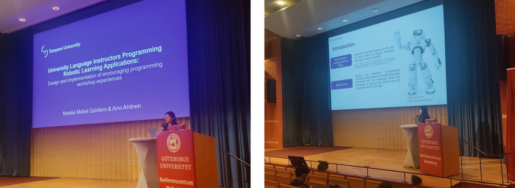 A woman is presenting at a conference. There is a big screen with a presentation on the back with the title of it.