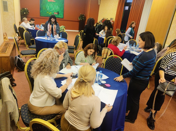 Ihmisiä istumassa huoneessa pyörien pöytien ympäröimänä.