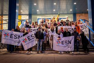 A large group of students standing on stairs with banderols. Text: ESN.
