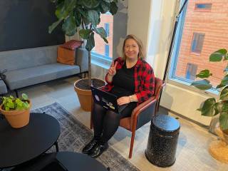 Nainen istuu tuolissa kannettava tietokone sylissä ja hymyilee.