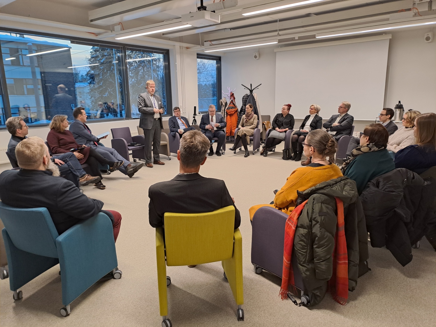 Ihmisiä istumassa tuoleissa ympyrämuodostelmassa ja rehtori Tapio Kujala seisomassa ja puhumassa ryhmälle.