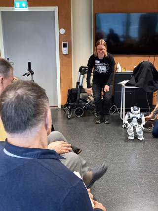 Kuvassa Nao-robotti on tekemässä liikesarjaa, jossa se koukistaa polviaan. Vieressä seisoo tutkija, joka tekee samaa koukistusliikettä.