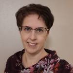 Hymyilevä silmälasipäinen lyhythiuksinen nainen katsoo suoraan kameraan.