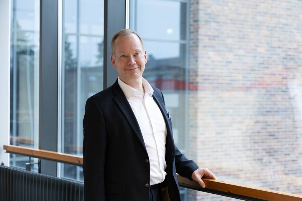 Tummaan pukuun pukeutunut mies käytävällä käsi kaiteella. 