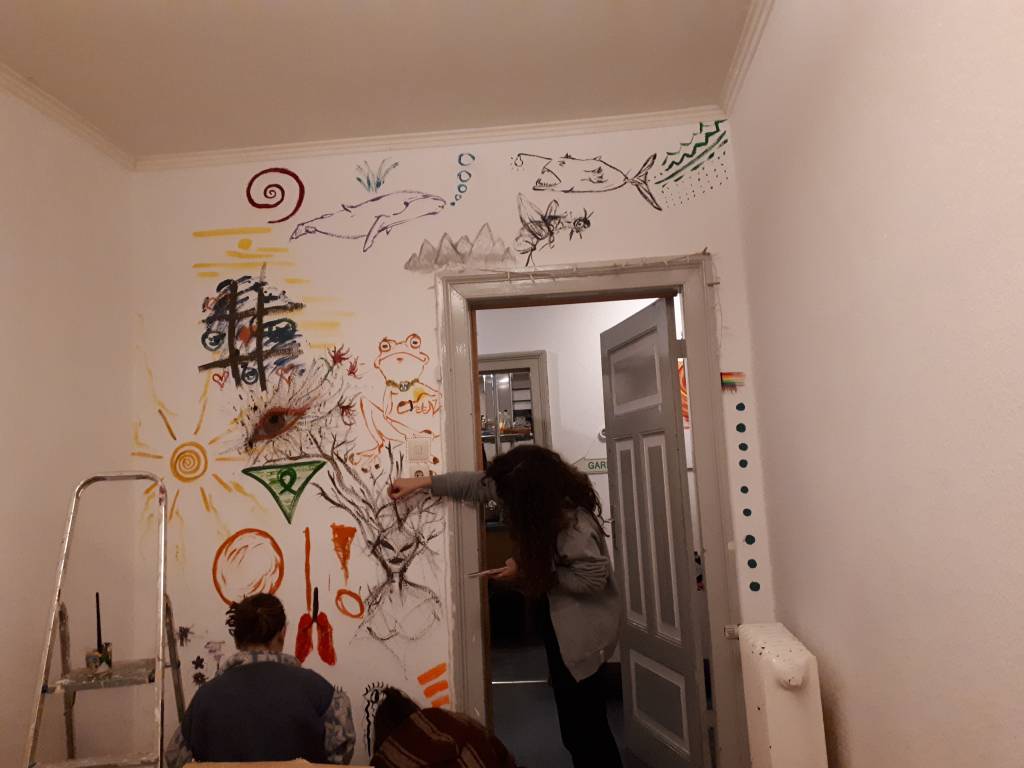 The people can be seen from the back, they are painting a white wall with colorful images.