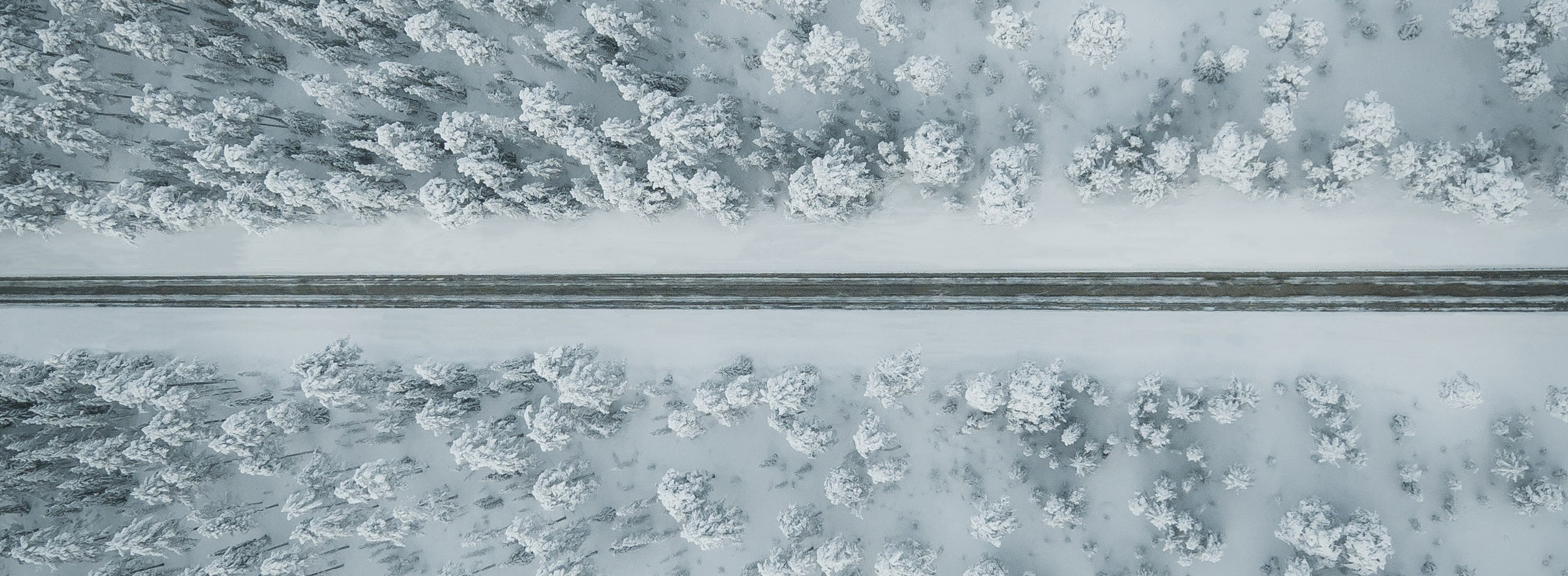 Talvinen maisema ylhäältäpäin kuvattuna, jossa keskellä tie ja ympärillä lumista metsää