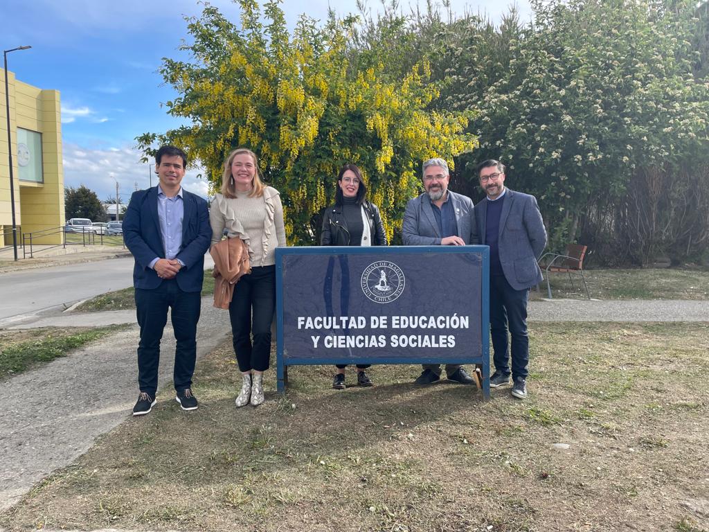 Five people standing outside behind a sign.