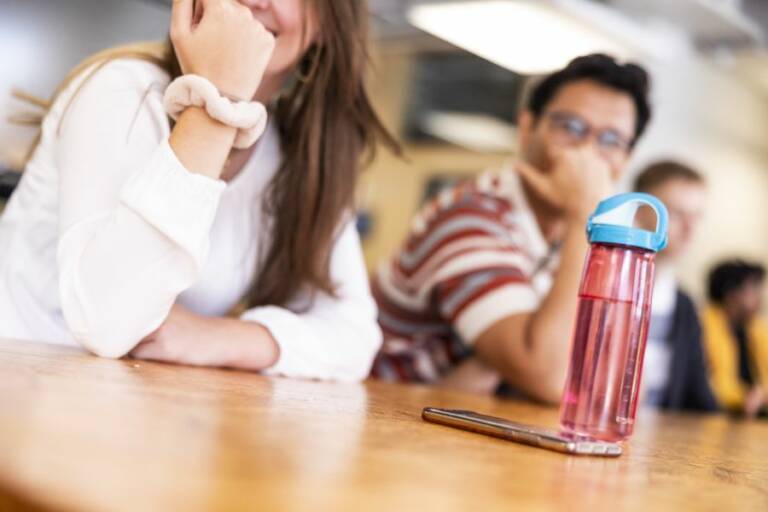 Opiskelijoita pöydän ympärillä käsi suun edessä