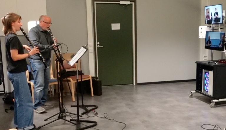 Kaksi klarinetin soittajaa sekä tietokoneruutuja.