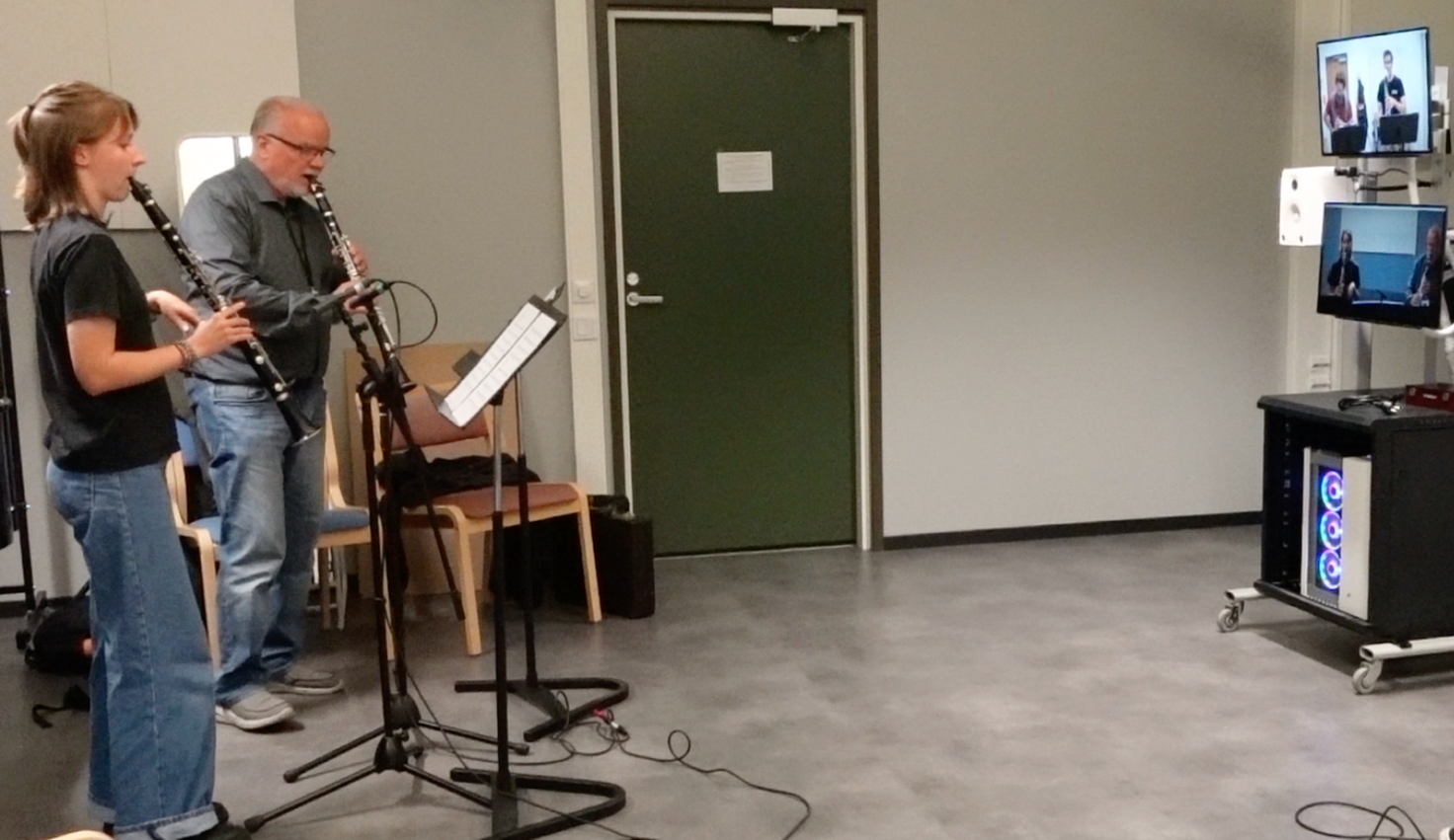 Kaksi klarinetin soittajaa sekä tietokoneruutuja.