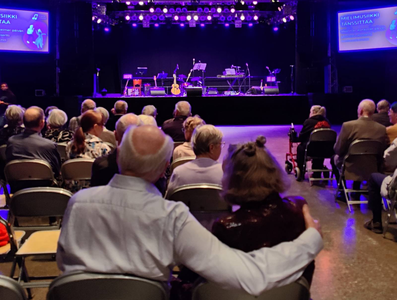 Elederly couple hugging each other and watching stage.
