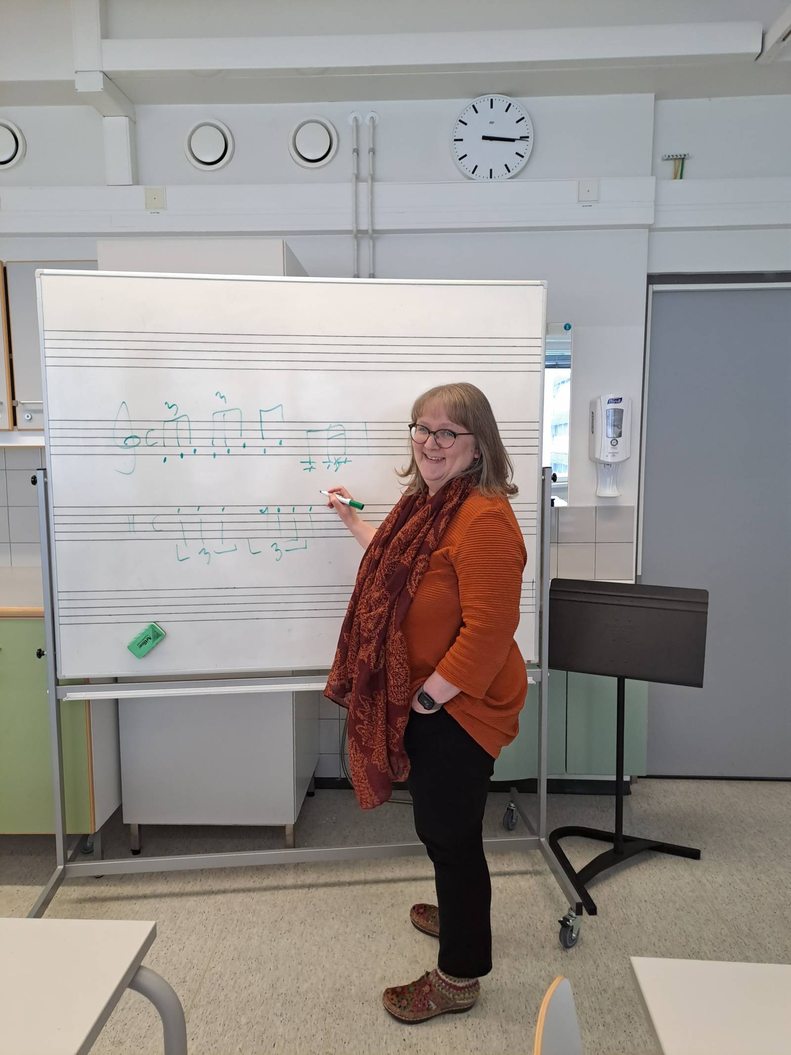 Susanna opettamassa nuottiviivastotaulun edessä.