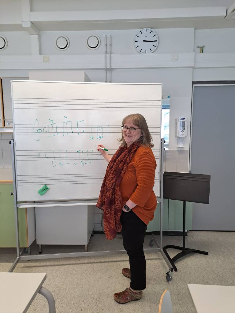 Susanna opettamassa nuottiviivastotaulun edessä.