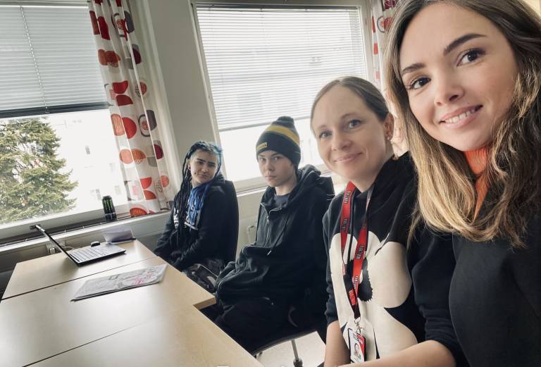 Kuvassa neljä opiskelijaa istuu pöydän ääressä.