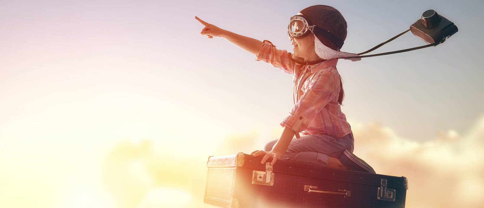 Pieni lapsi, jonka oikea käsi osoittaa suorana eteenpäin, lentää taivaalla matkalaukun päällä.