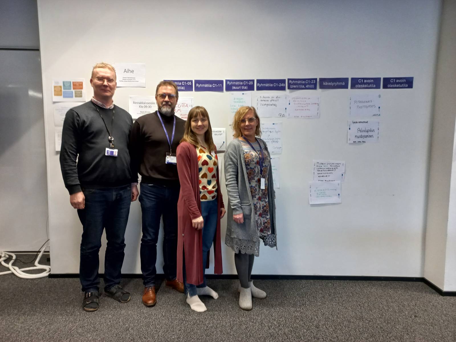 Neljä henkilöä seisomassa seinän edessä.