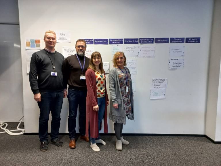 Neljä henkilöä seisomassa seinän edessä.