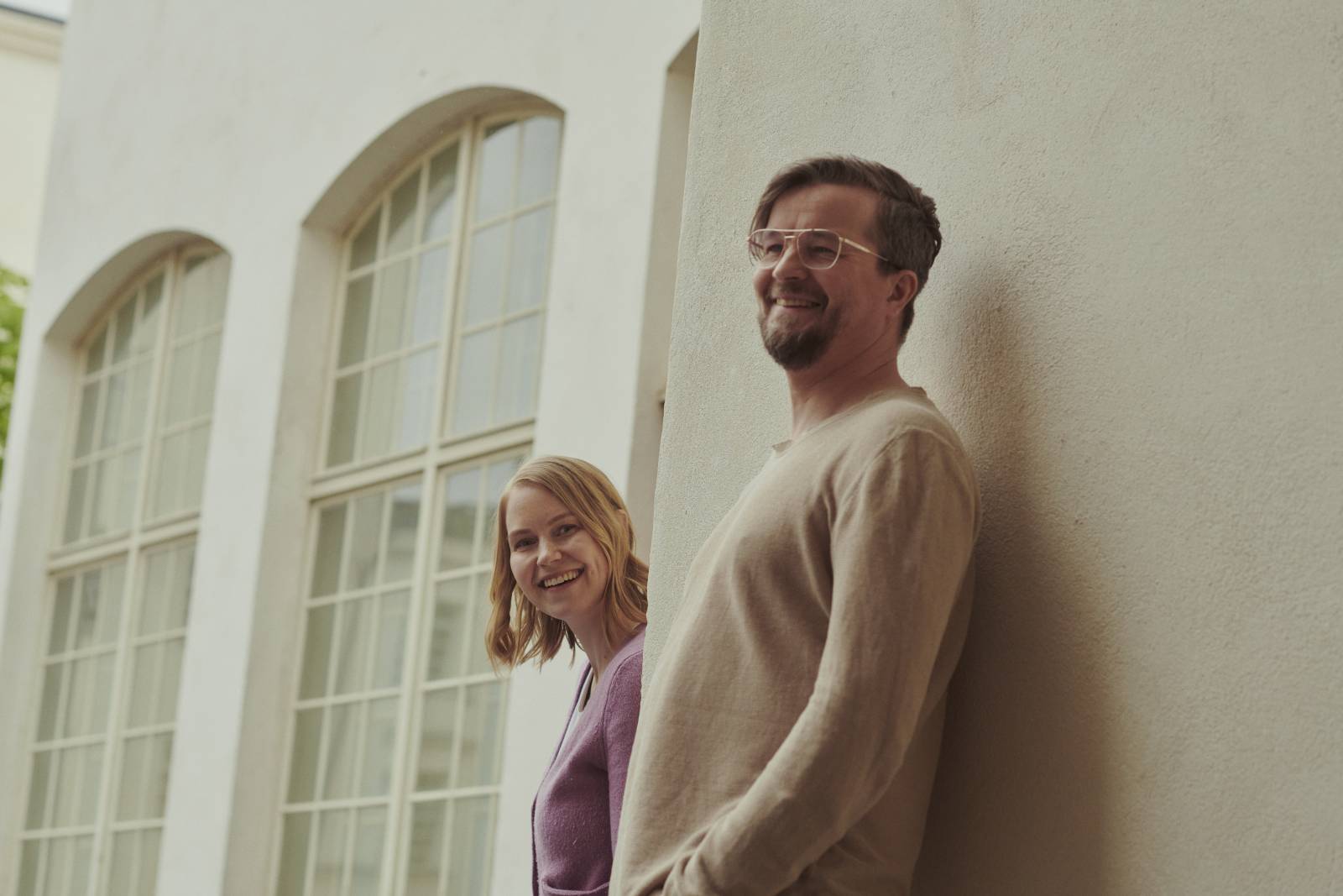 Kaksi hymyilevää ihmistä nojaa seinään.