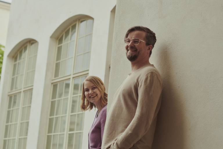 Kaksi hymyilevää ihmistä nojaa seinään.