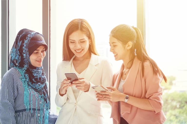 Kolme hyväntuulista opiskelijanaista juttelee ja katselee puhelimiaan.