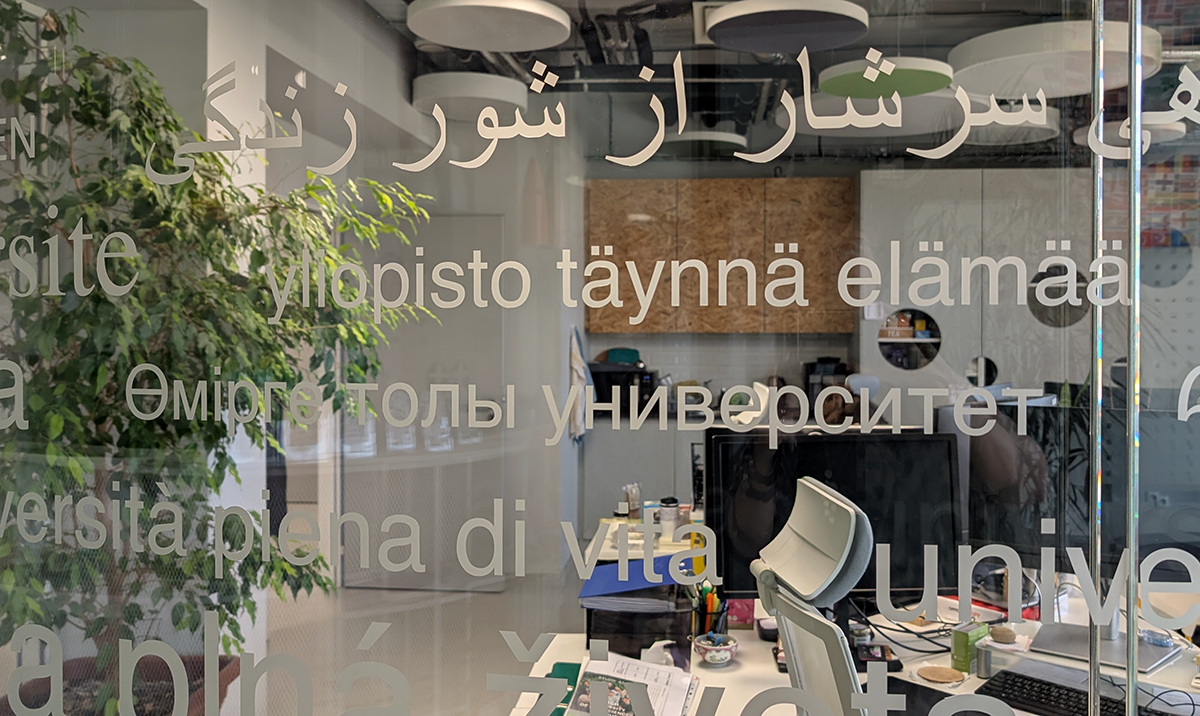 Lasiseinässä teksti "Yliopisto täynnä elämää" eri kielillä.
