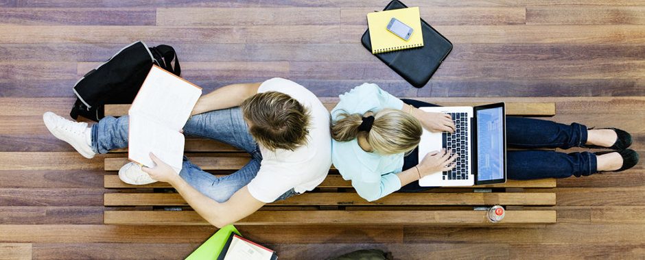 Kaksi henkilöä opiskelee selät vastakkain lattialla istuen.