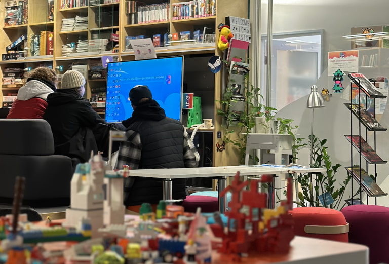 A photo of OASIS where three students play a game on a big screen.