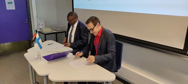 Two men sitting around the table and signing papers.