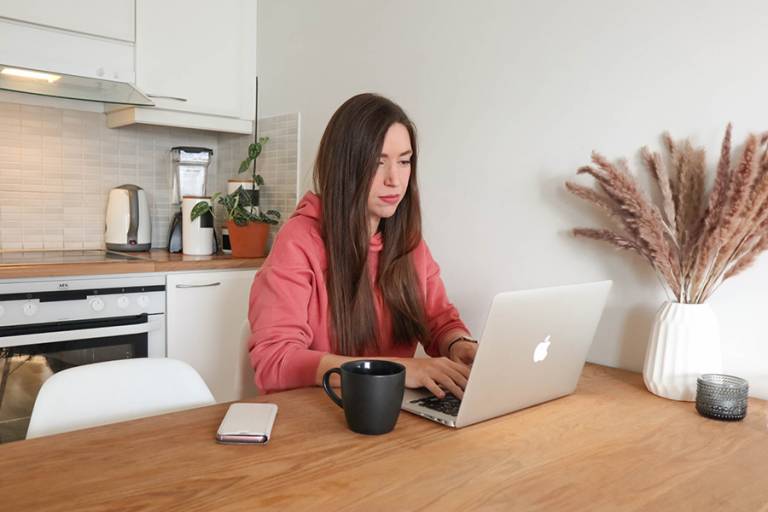 Tyttö istuu keittiössä läppärin ääressä.